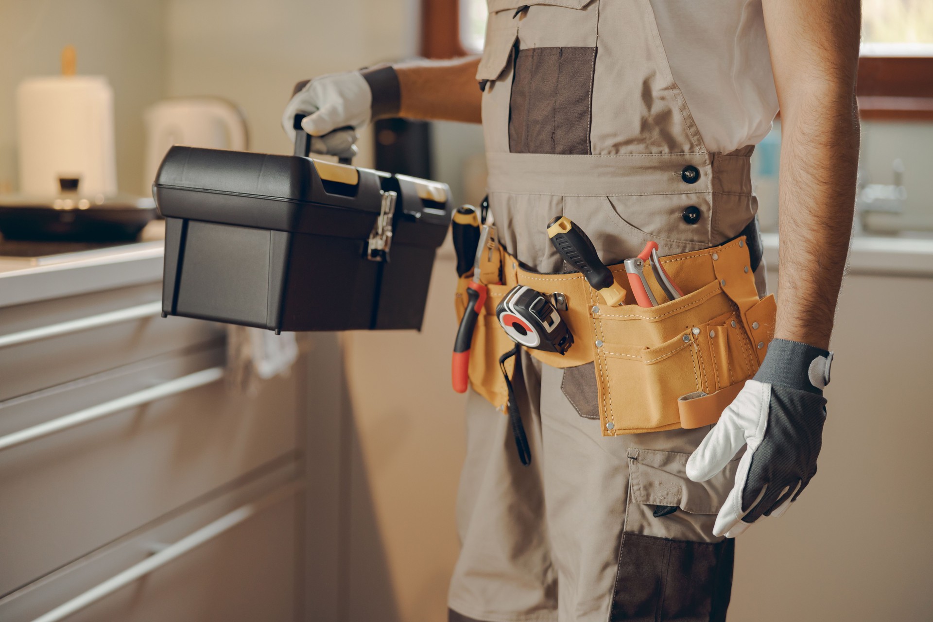 Nahaufnahme eines Mechanikers in Uniform, der in der heimischen Küche steht und seine Werkzeugtasche hält