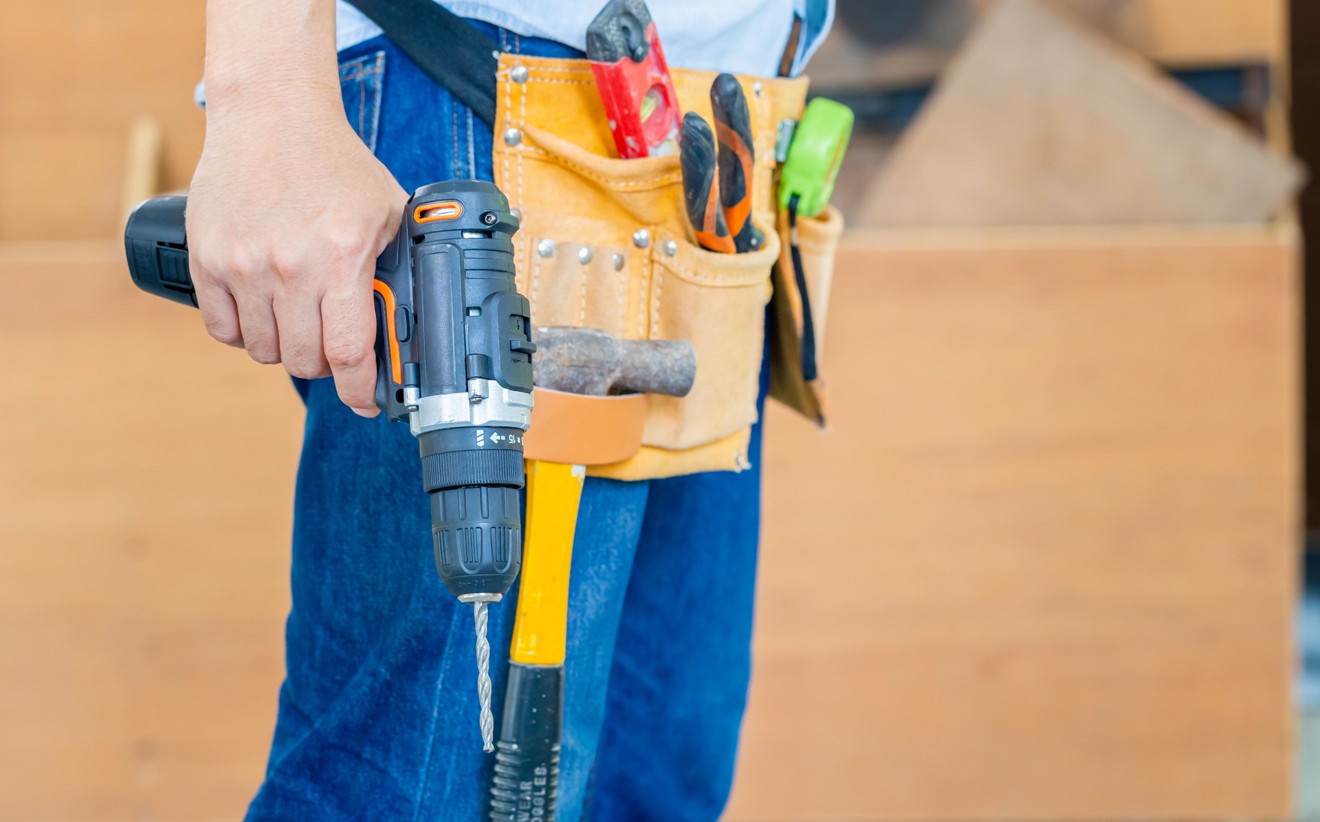 Handyman manual worker in tools belt and holding drill in his hands, Carpenter working with equipment in wood workshop, man doing woodwork in carpentry shop