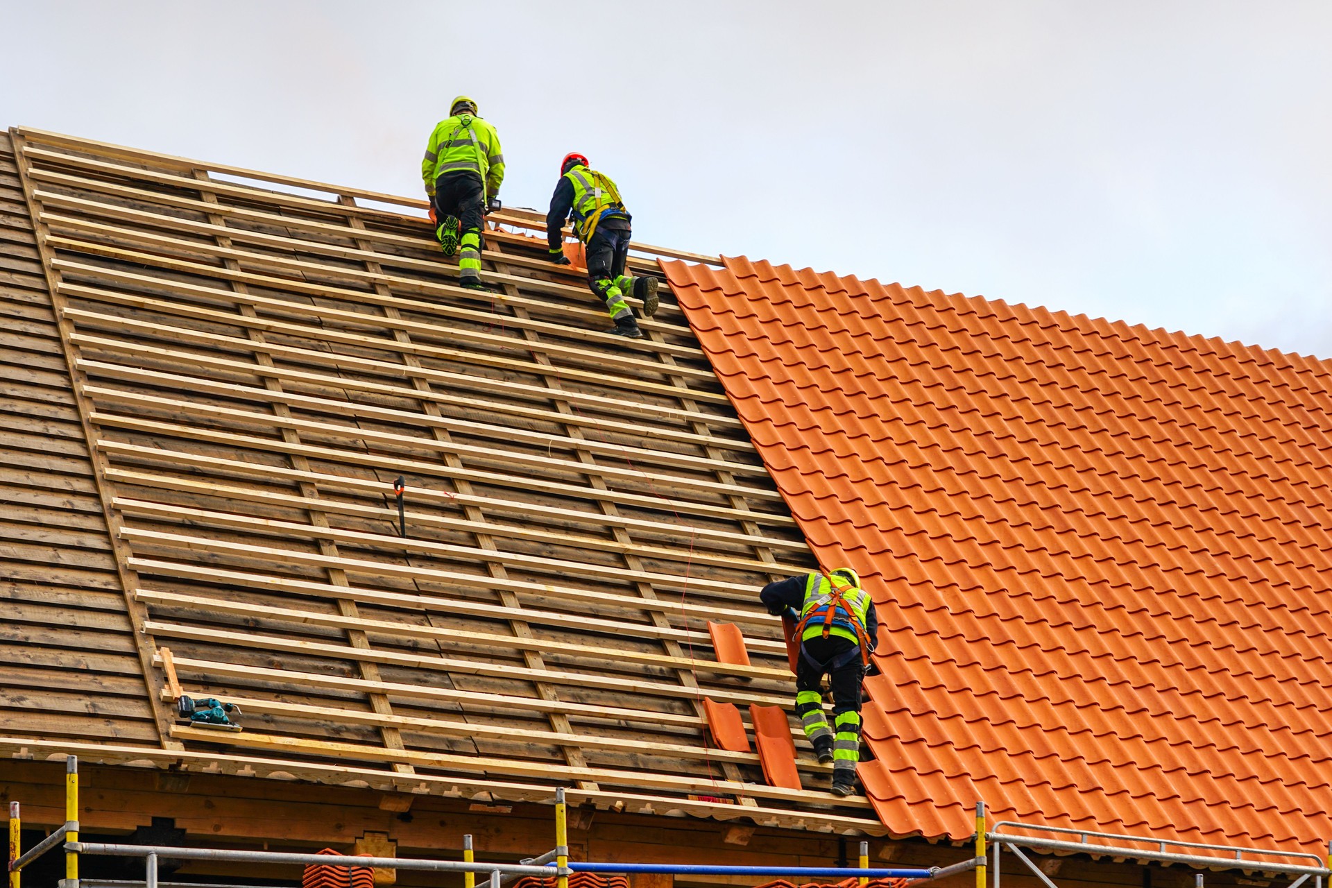 Drei Dachdecker in Arbeitsschutzkleidung verlegen neue Tonziegel, neue Tonziegelschichten